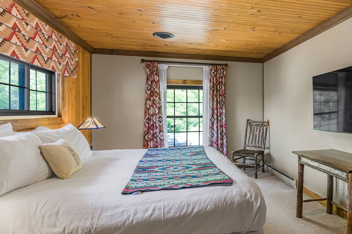 A bedroom with a bed, a chair, a desk, a television, and a refrigerator.