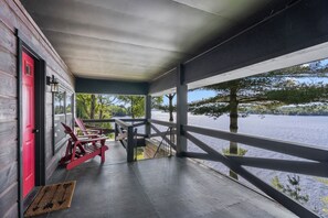 A covered porch with a red door, wooden railings, and a view of a lake.