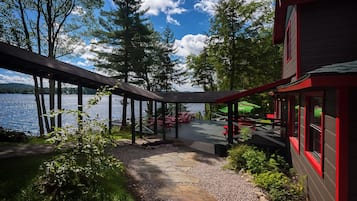 A lakeside deck with a stone pathway leading to outdoor seating, surrounded by trees and a building with red trim.