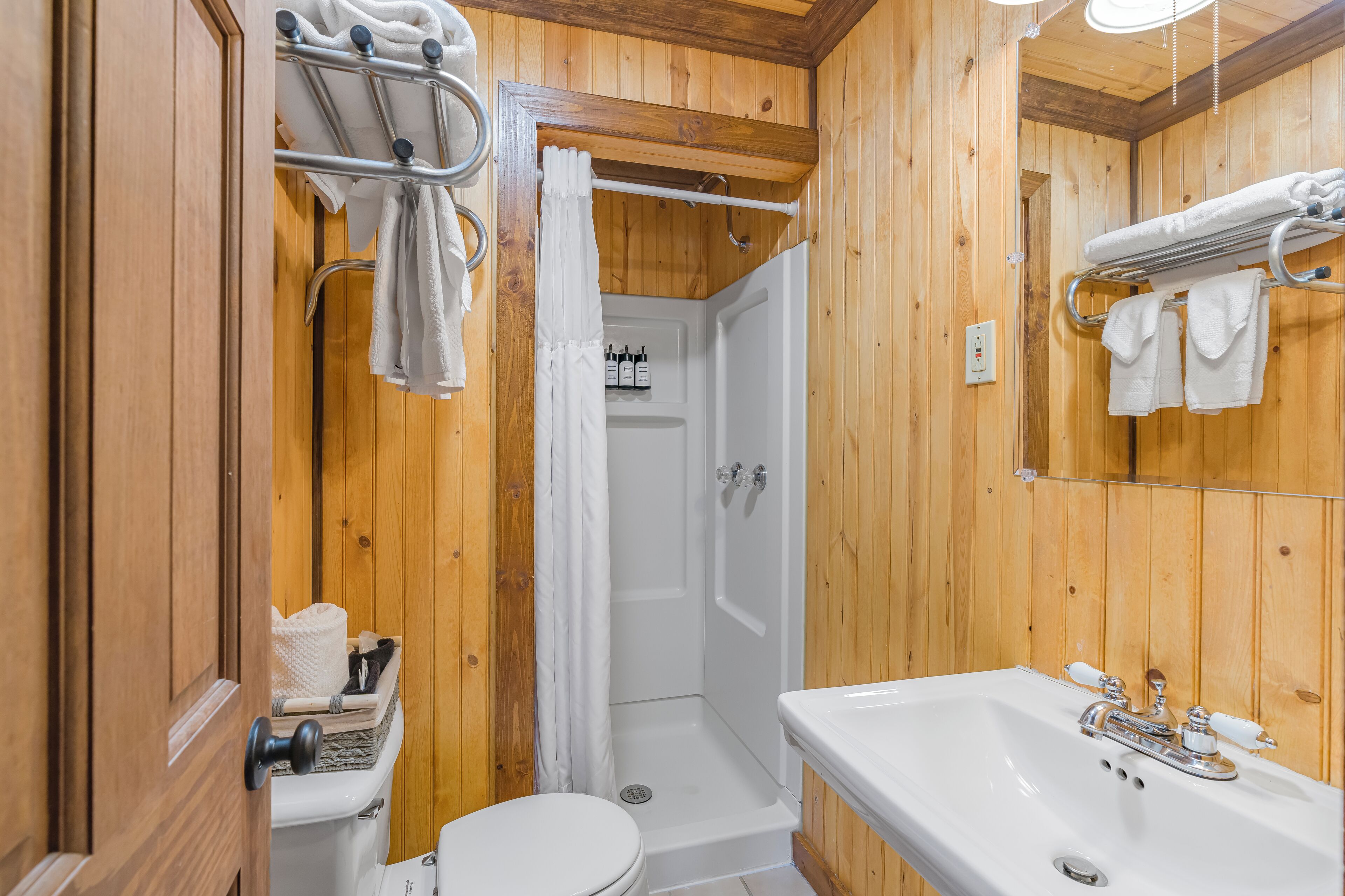 A wooden-paneled bathroom with a toilet, sink, and shower.