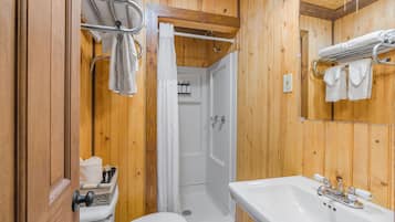 A wooden-paneled bathroom with a toilet, sink, and shower.