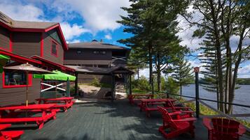 A deck with red Adirondack chairs and picnic tables, overlooking a lake.