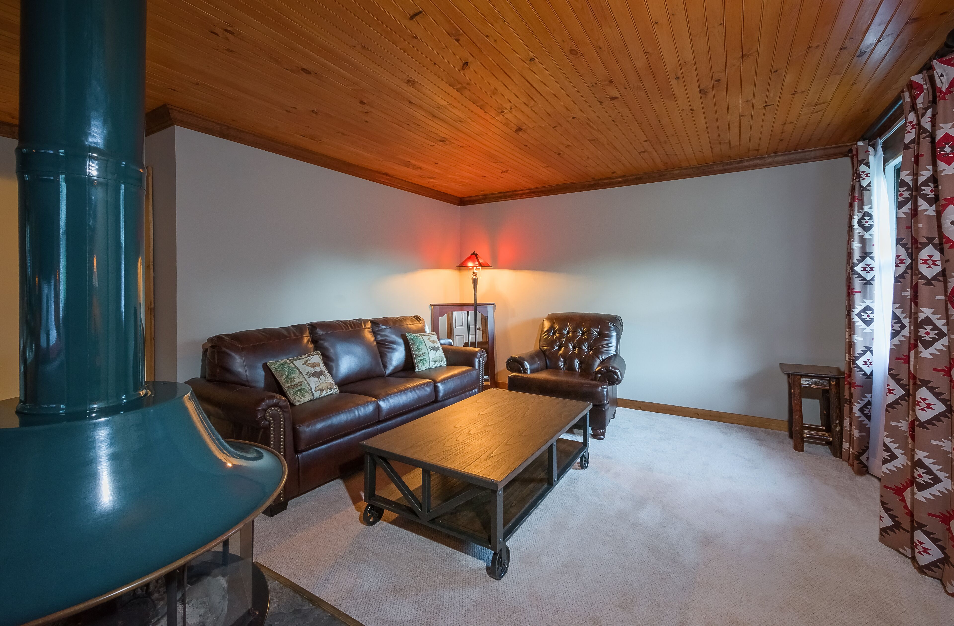 Un salon chaleureux avec un plafond en bois, un canapé en cuir marron, une table basse en bois et une cheminée de couleur turquoise.