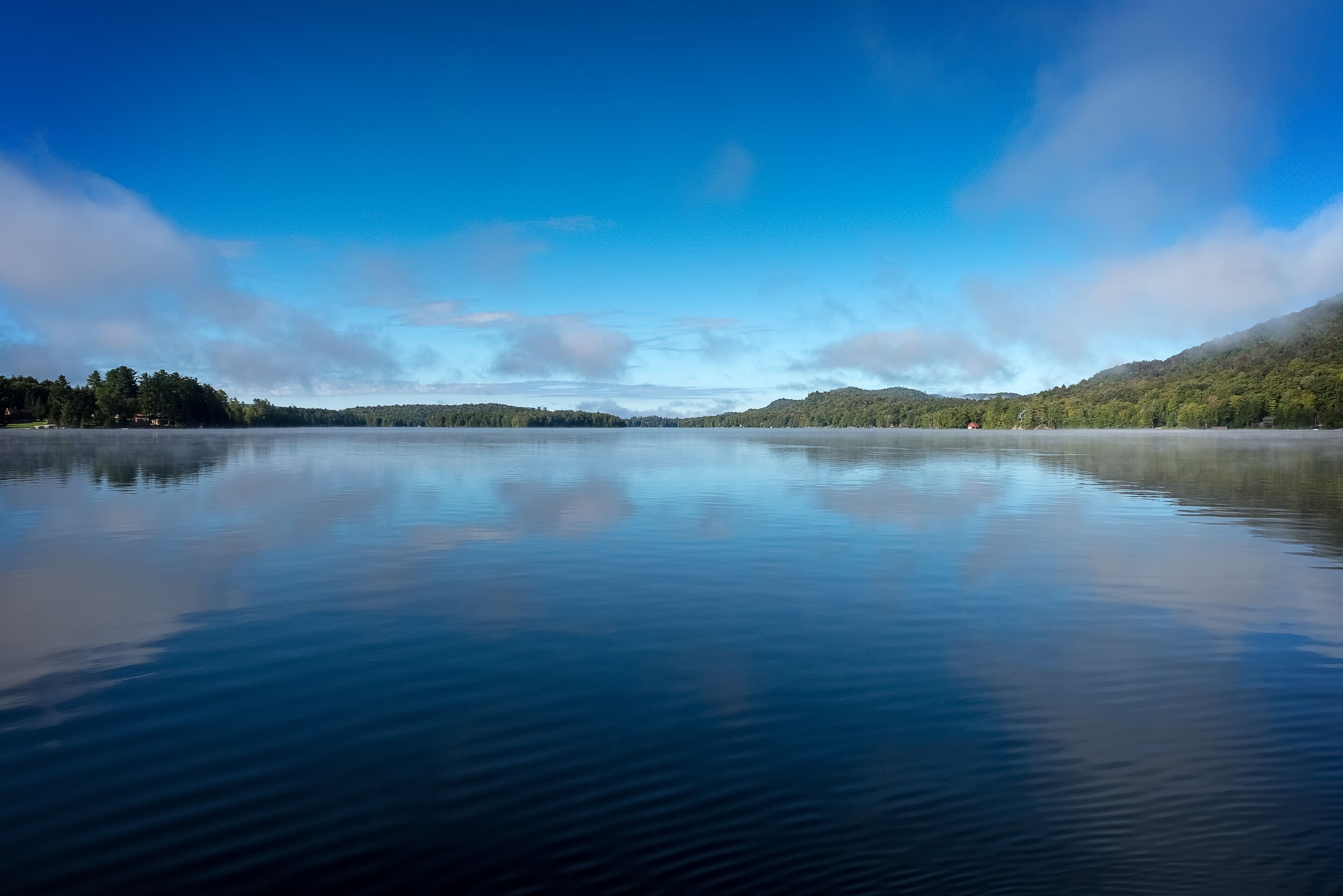 Un lago tranquilo con cielo despejado y colinas lejanas.