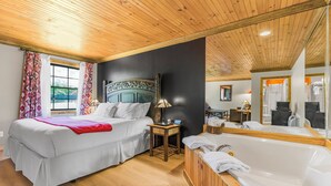 Un dormitorio con una cama grande, techo de madera, bañera y ventana con cortinas.