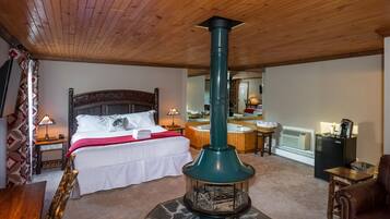 Une pièce confortable avec un lit, un plafond en bois, une cheminée en pierre, une salle de bain avec baignoire et un réfrigérateur.