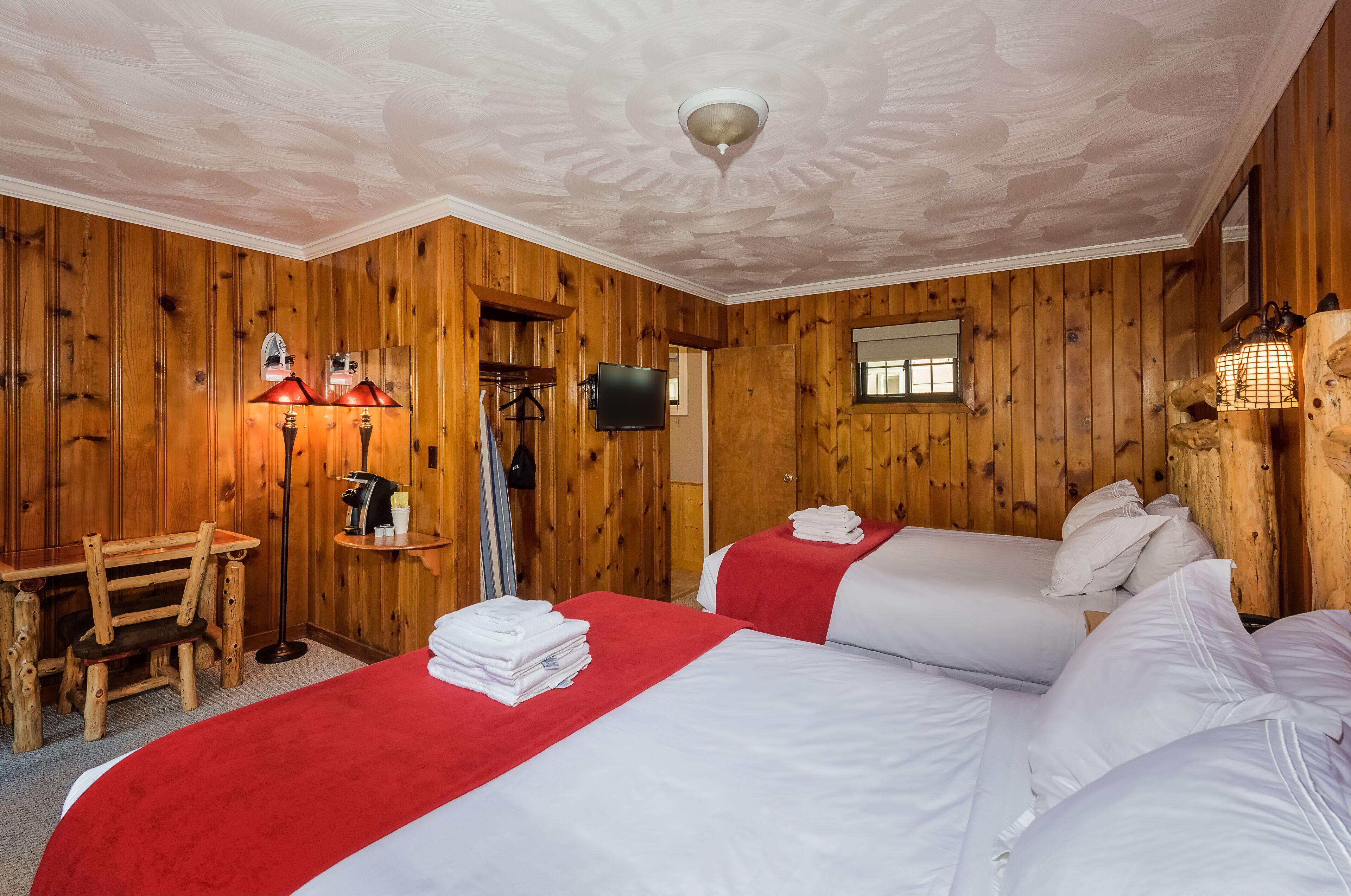 Ein Zimmer mit Holzwänden, zwei Betten, einem Schreibtisch und einem Fernseher.