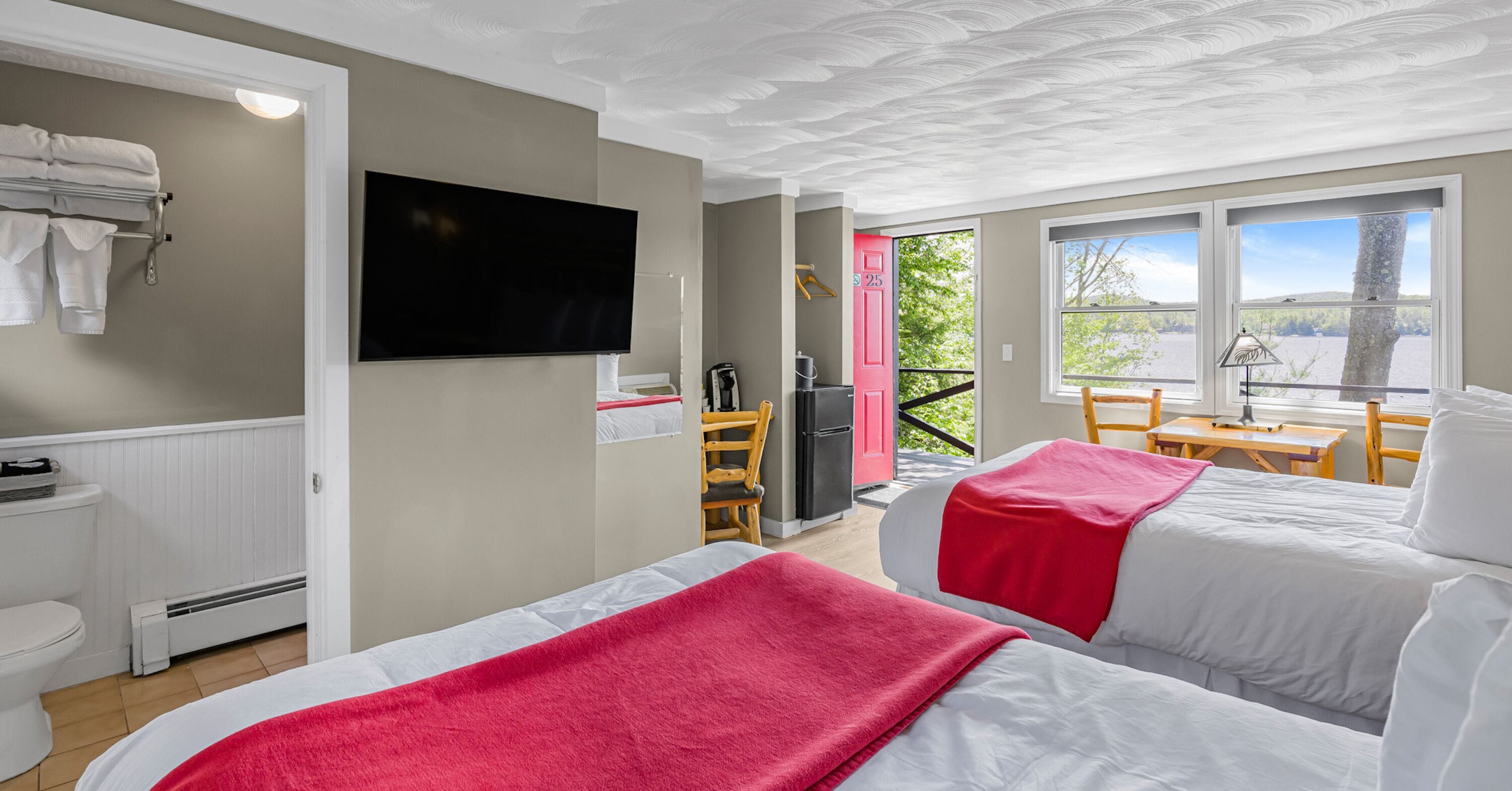 Habitación de hotel con dos camas, televisor, balcón con vistas y puerta roja.