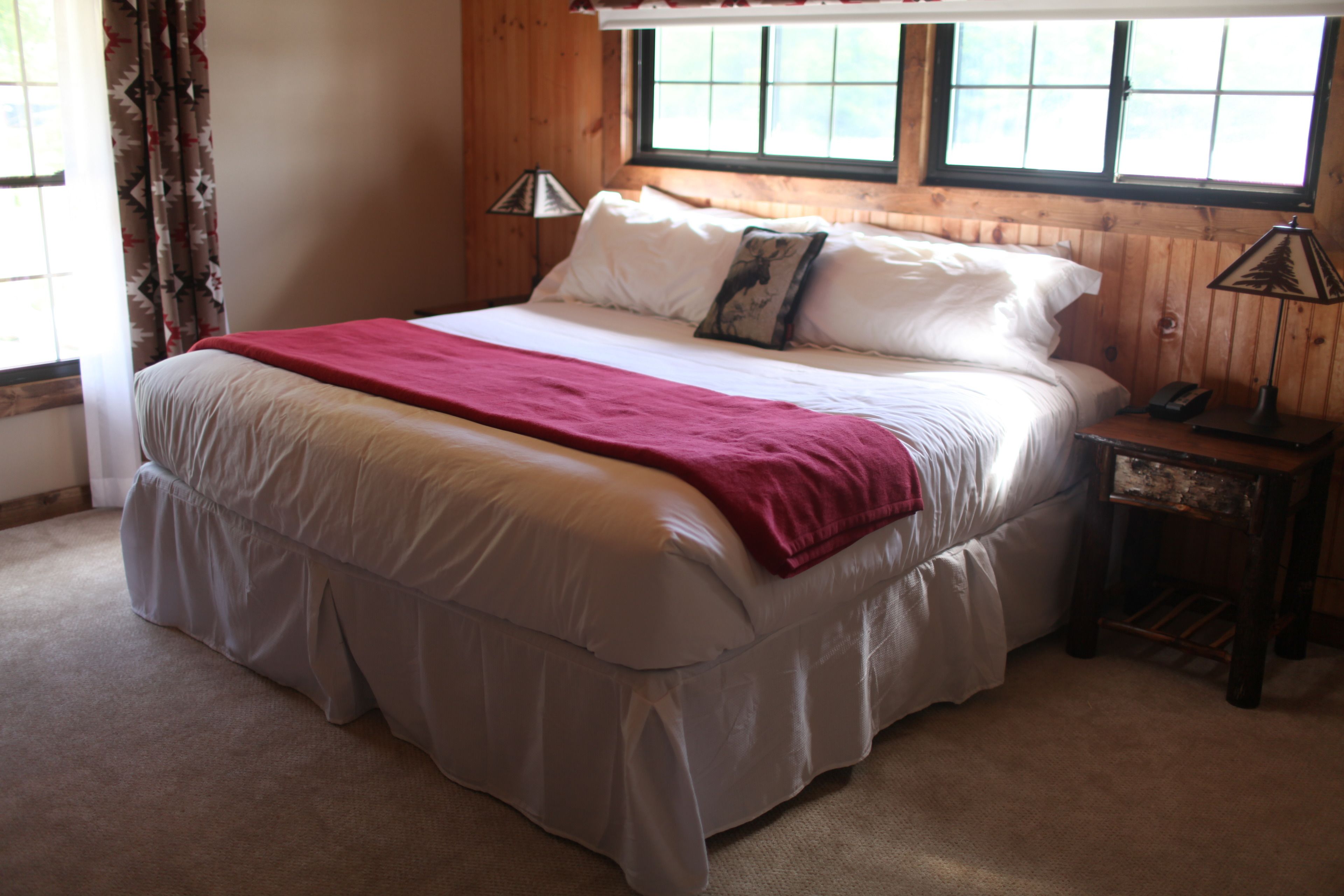 A bedroom with a large bed, a bedside table with a lamp, and a window with curtains.