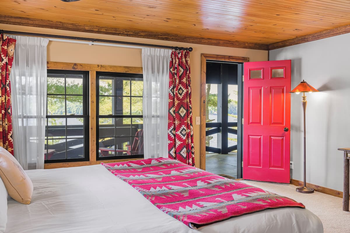 A bedroom with a bed, a red door, and a view through a glass door to an outdoor area.