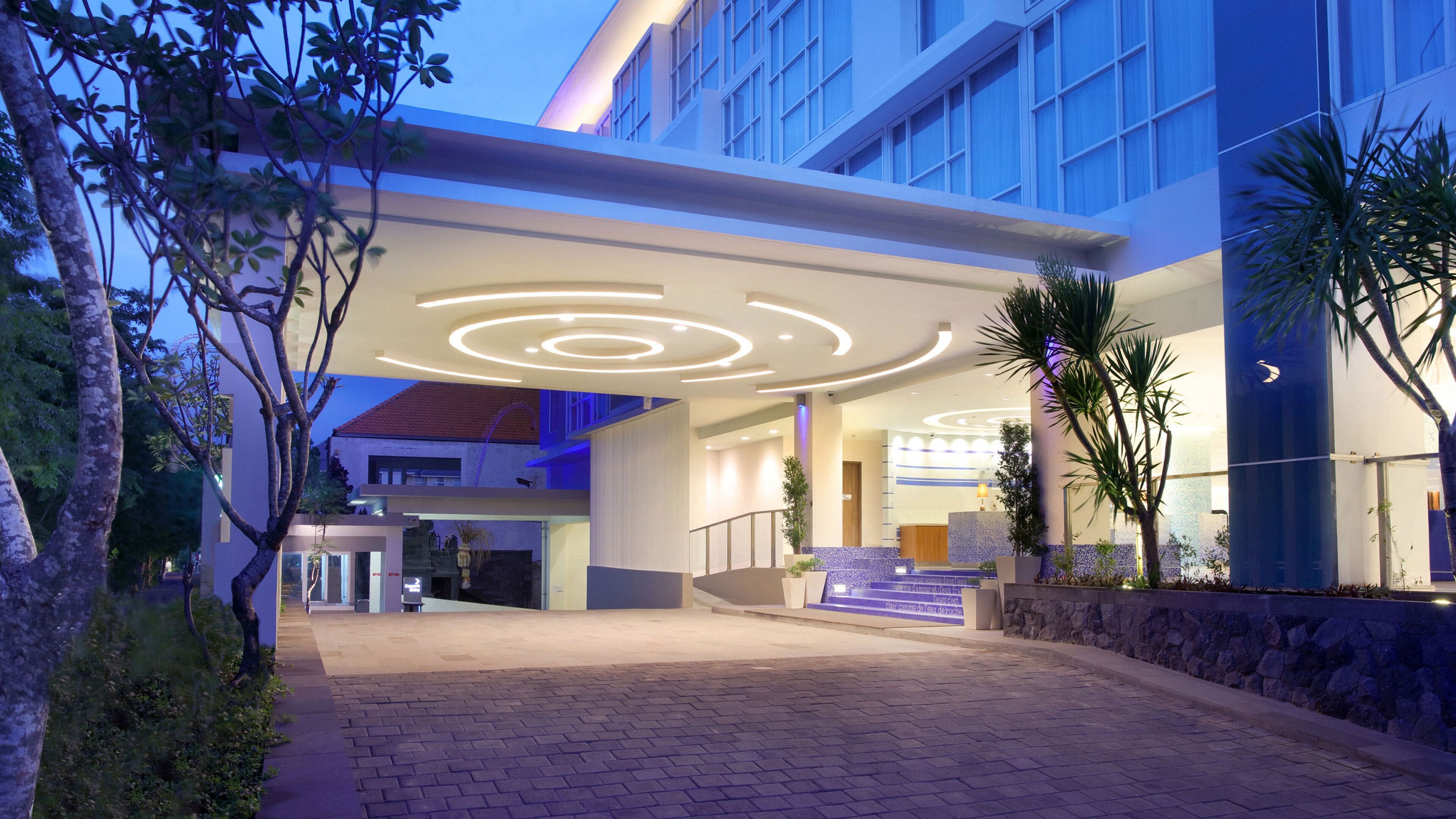 A modern hotel entrance with a circular light design on the ceiling, a stone wall, and a staircase leading to the lobby.