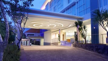 A modern hotel entrance with a circular light design on the ceiling, a stone wall, and a staircase leading to the lobby.