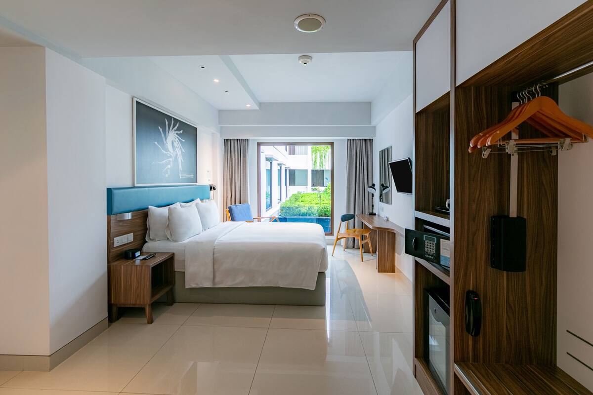 A modern hotel room with a large bed, a desk, a TV, and a view of the outside.