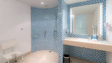 Un baño con pared de mosaico azul, un lavabo blanco, un espejo y una silla blanca.