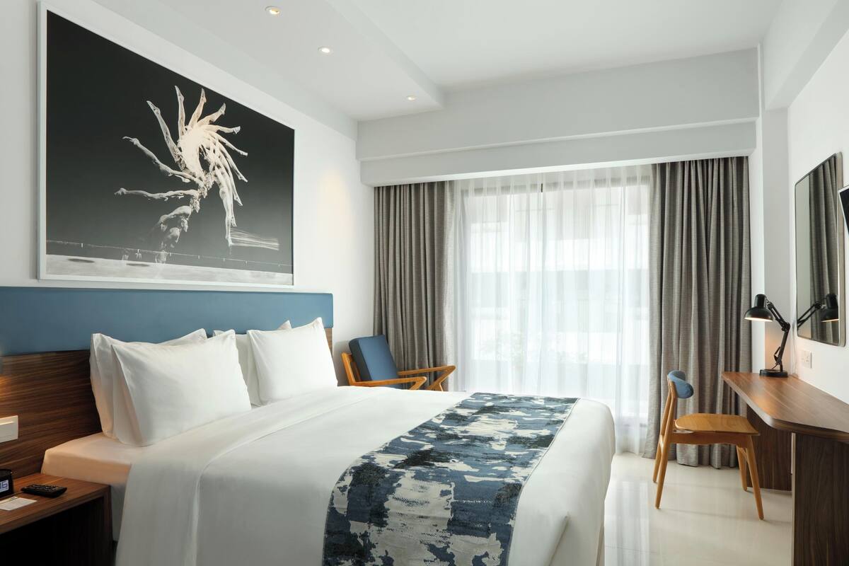 A hotel room with a large bed, a desk with a chair, a TV, and a window with curtains.