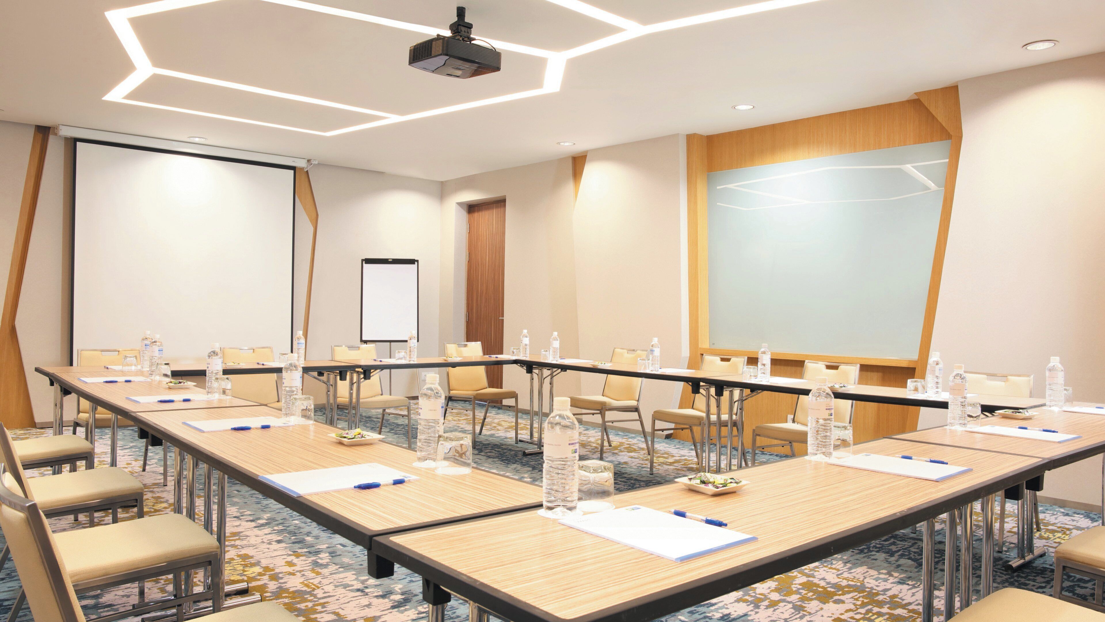 A conference room with a long table, chairs, water bottles, and a projector screen.