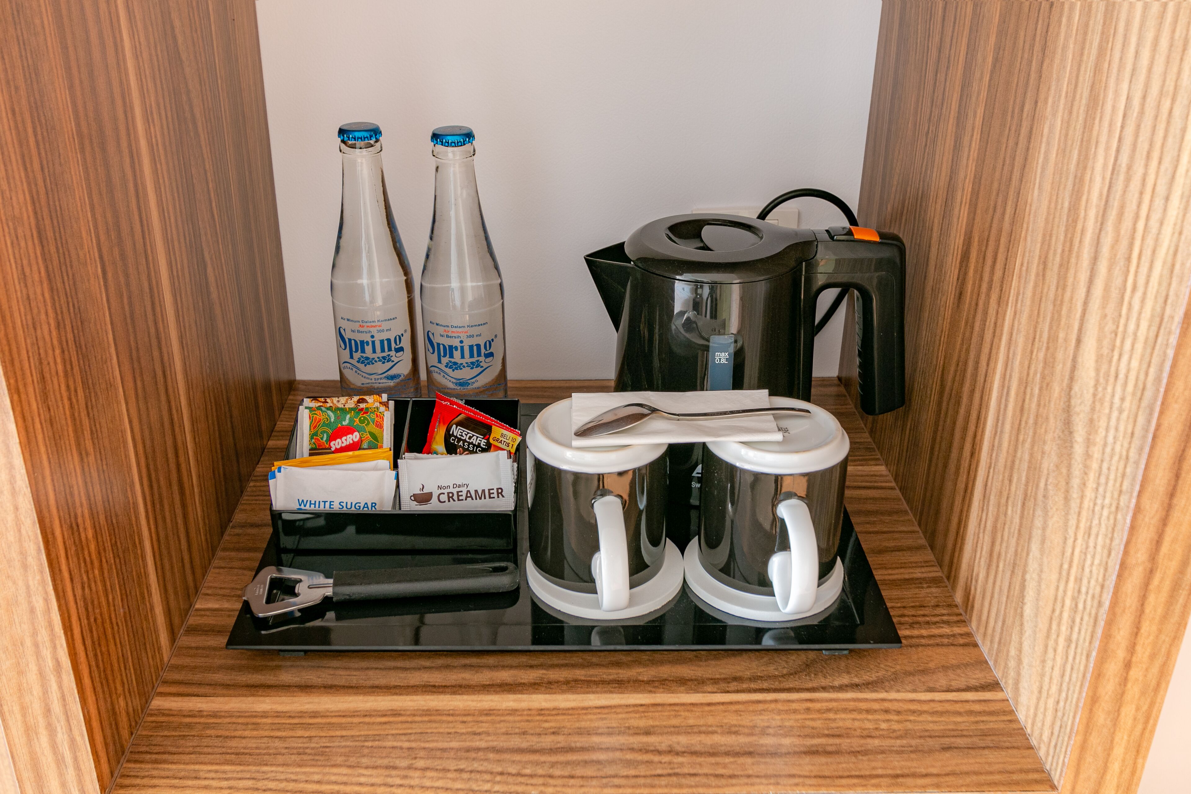 A kitchen area with two bottles of Spring water, a coffee maker, a kettle, and a creamer dispenser.