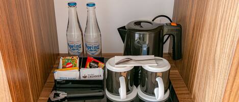 Una kitchenette con dos botellas de agua Spring, una cafetera, un hervidor y un dispensador de leche.