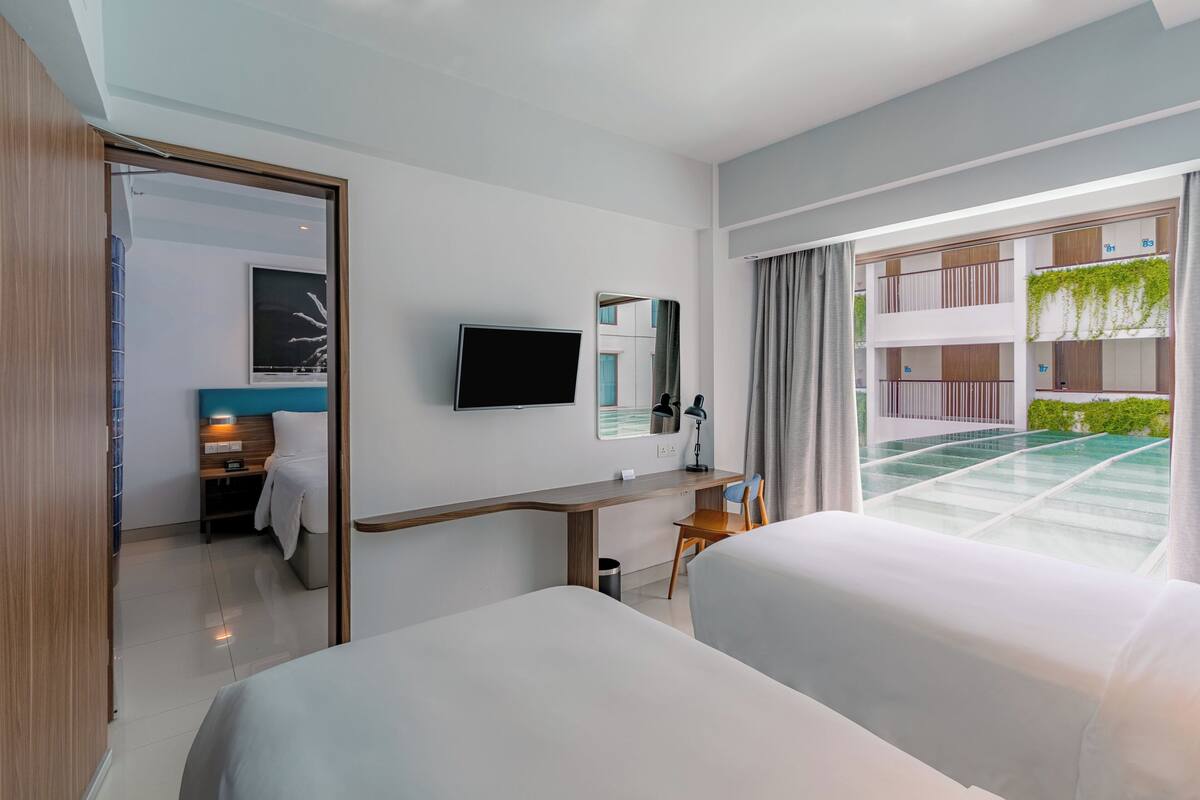 A hotel room with two beds, a desk, a TV, and a view of the outdoor balcony.