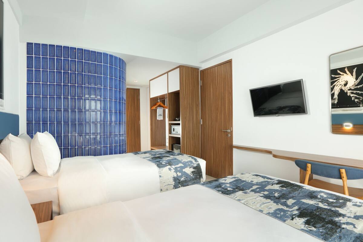 A hotel room with two beds, a TV, a wardrobe, and a bathroom with blue tiles.