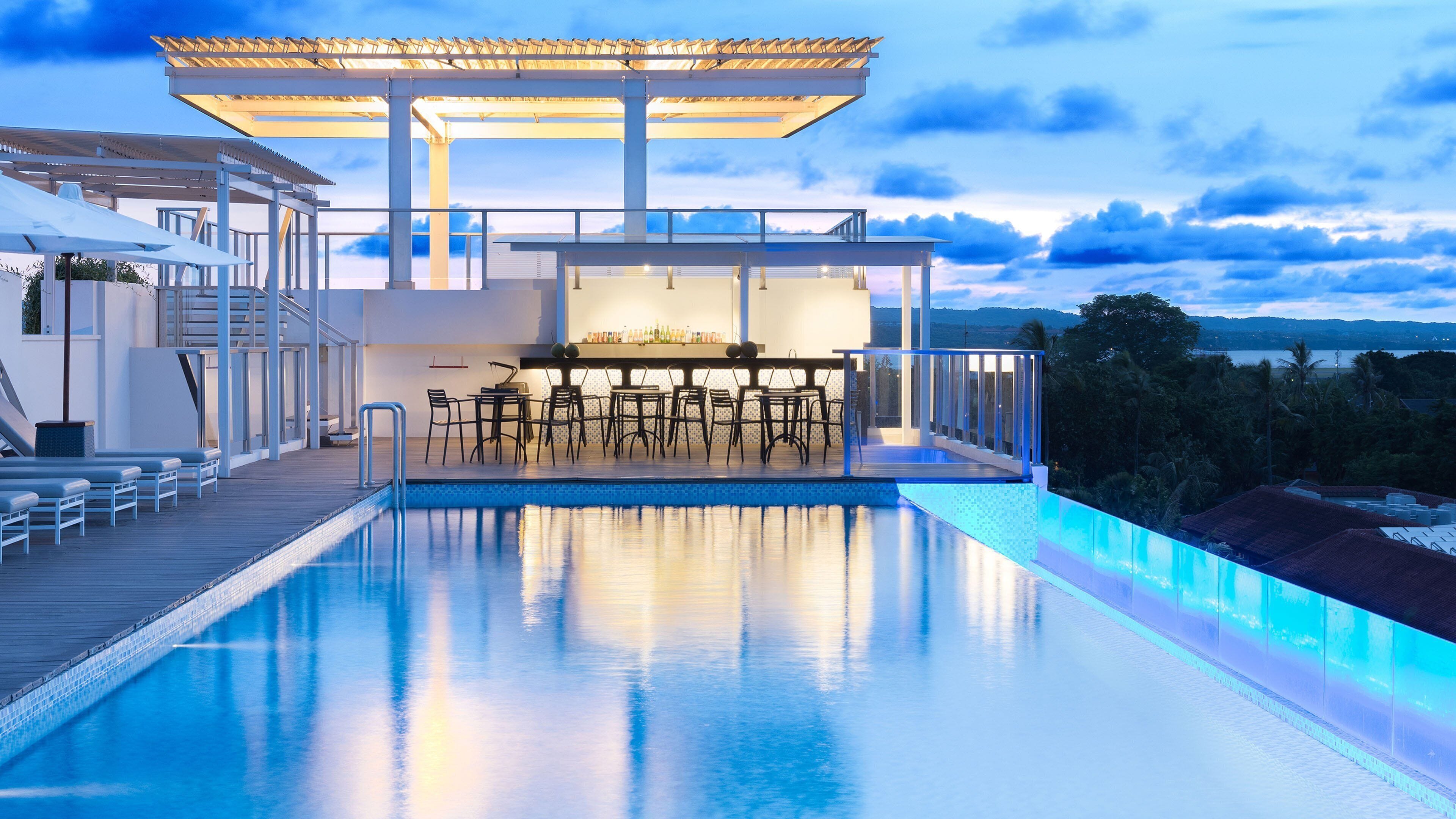 A modern outdoor pool area with a bar and seating, surrounded by a wooden deck and overlooking a landscape.