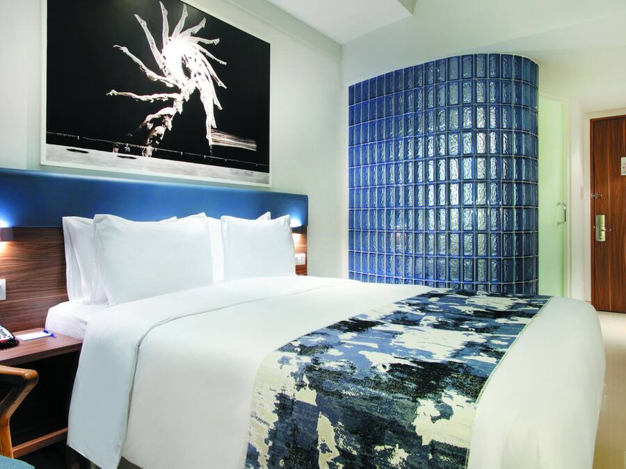 A hotel room with a large bed, a desk with a telephone, a wall-mounted light, and a door with a sign.