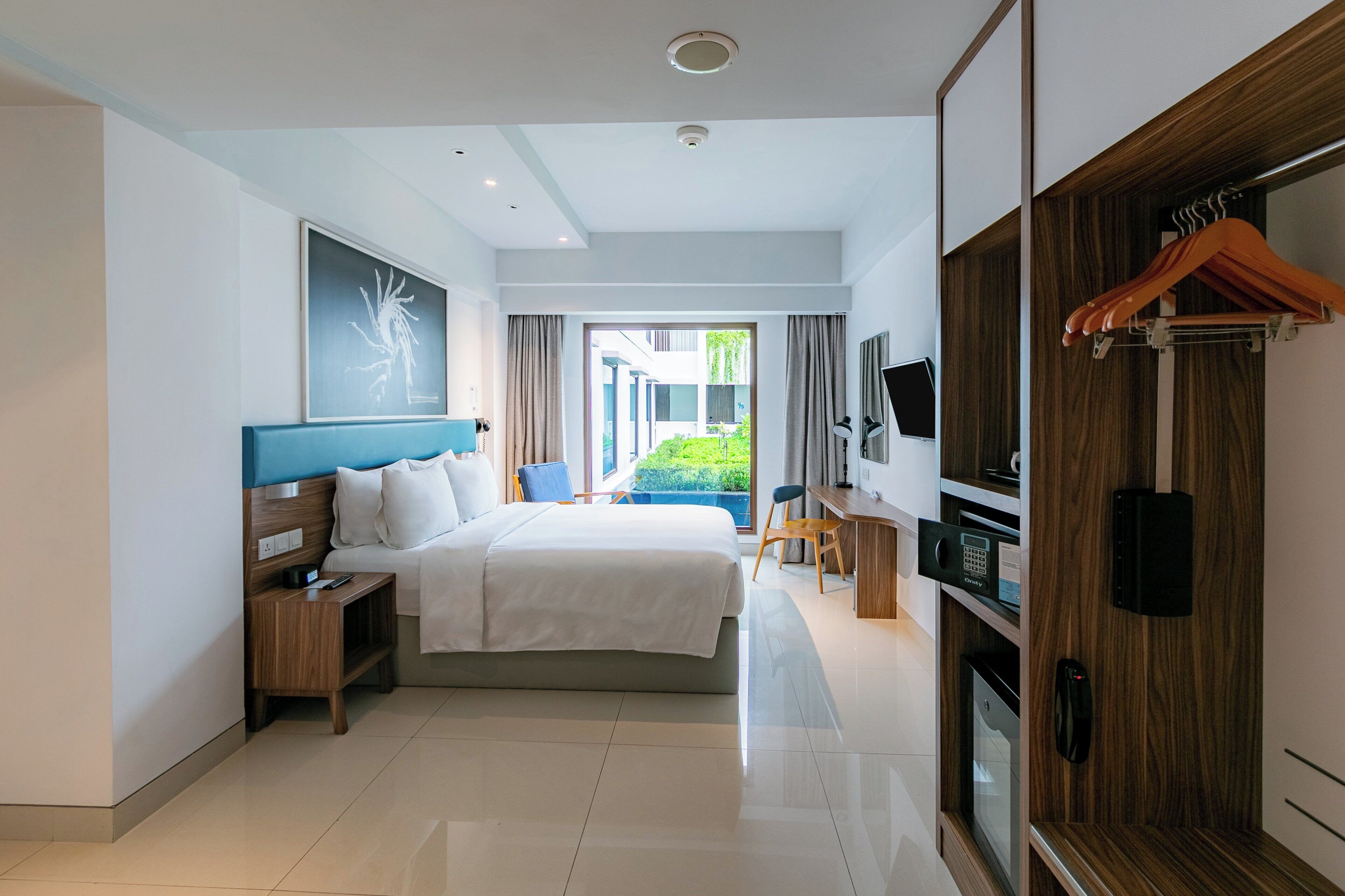 A hotel room with a bed, bedside tables, a desk, a TV, and a wardrobe.