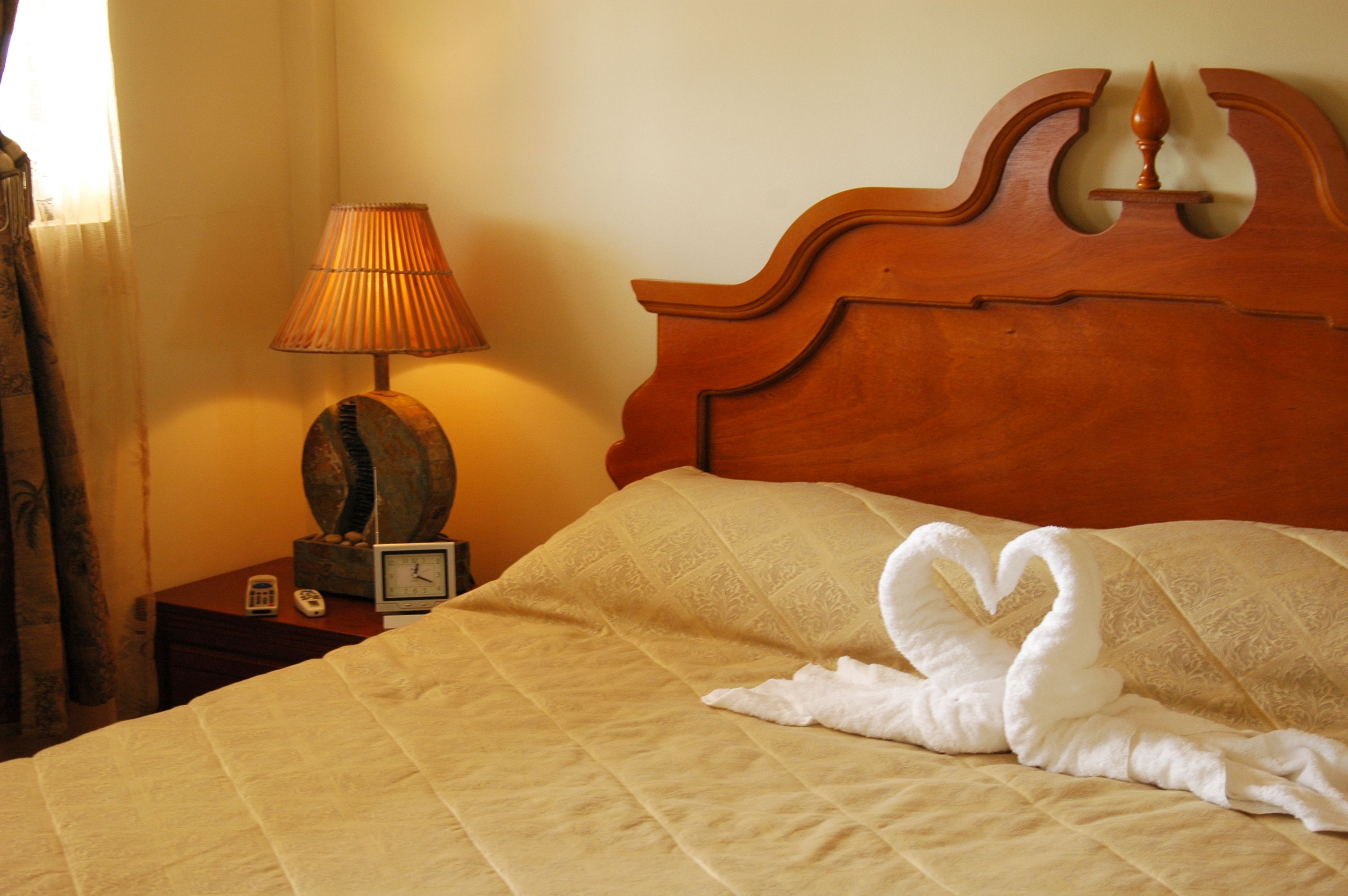 Una camera d'albergo con un letto, una testiera in legno, una lampada e una sveglia su un comodino.