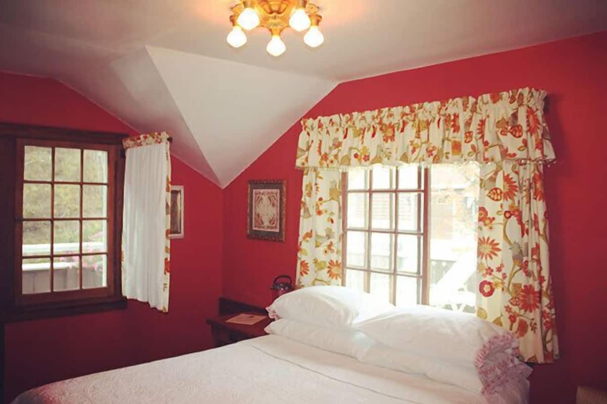 Une chambre à coucher avec un grand lit, une fenêtre ornée de rideaux à motifs floraux, une table de chevet et un luminaire au plafond.