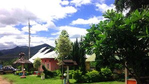 Une maison de campagne à l’extérieur rouge, entourée d’une végétation luxuriante et sous un ciel dégagé.