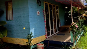 Une petite maison à un seul étage, à l’extérieur bleu, avec un toit de chaume et un porche doté d’un banc.