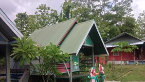Une rangée de petites cabanes à un seul étage, dotées de toits verts, entourées d’une végétation luxuriante et d’arbres.