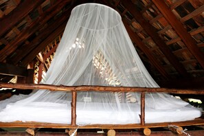 Un lit doté d’un baldaquin blanc et de poutres en bois au plafond.