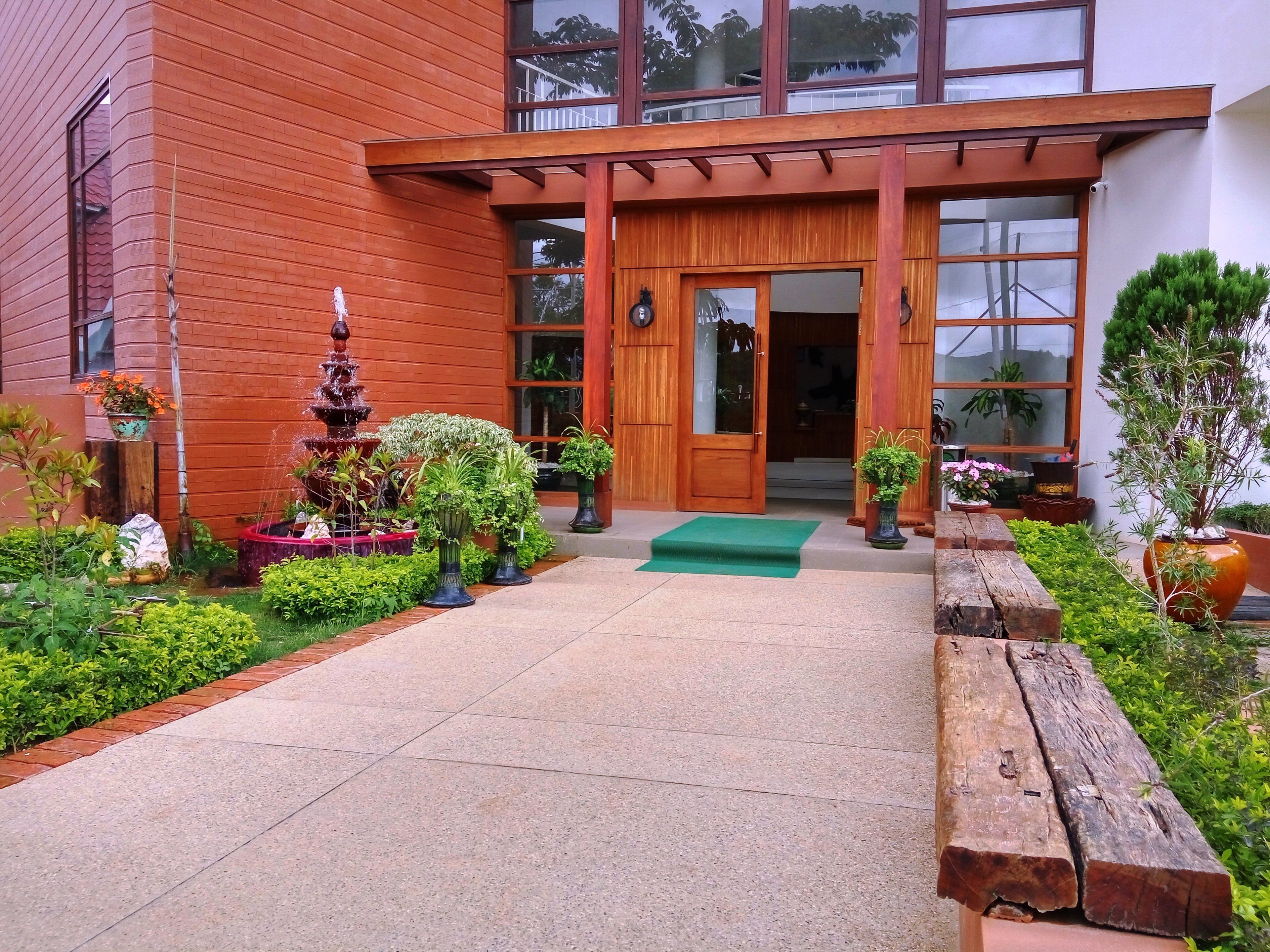 A building with a wooden facade, a front entrance with a green mat, and a small garden with a fountain and potted plants.