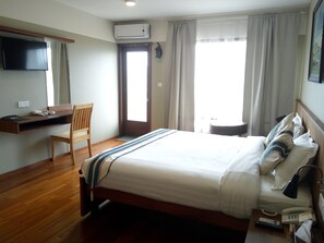 A hotel room with a bed, a desk with a chair, a TV, an air conditioner, a window with curtains, and a bedside table with a lamp and a phone. - 360 Kalaw Hotel (Kalaw)