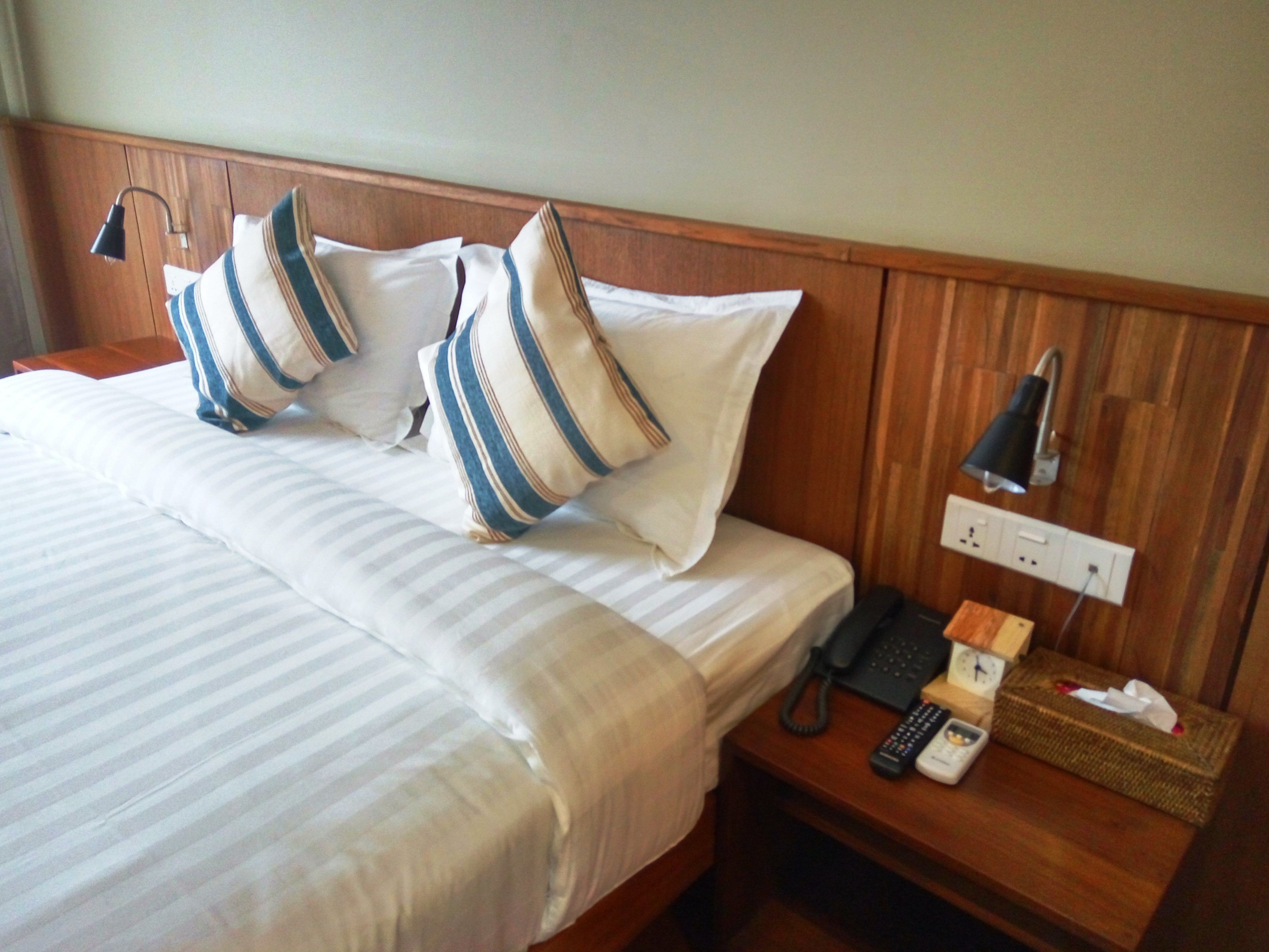 A neatly made bed with striped bedding and two pillows, a bedside table with a lamp, a phone, and a tissue box.