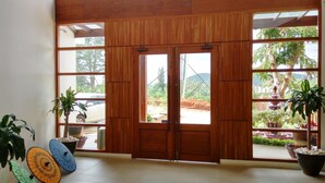 Puerta de madera con paneles de vidrio, plantas en macetas y piso de baldosas.