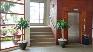Un interior moderno con una escalera, plantas en macetas y un ascensor metálico.