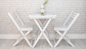 A white table with two white chairs, a white vase with a plant, and a white brick wall. - James Place @ Dowlais (Merthyr Tydfil)