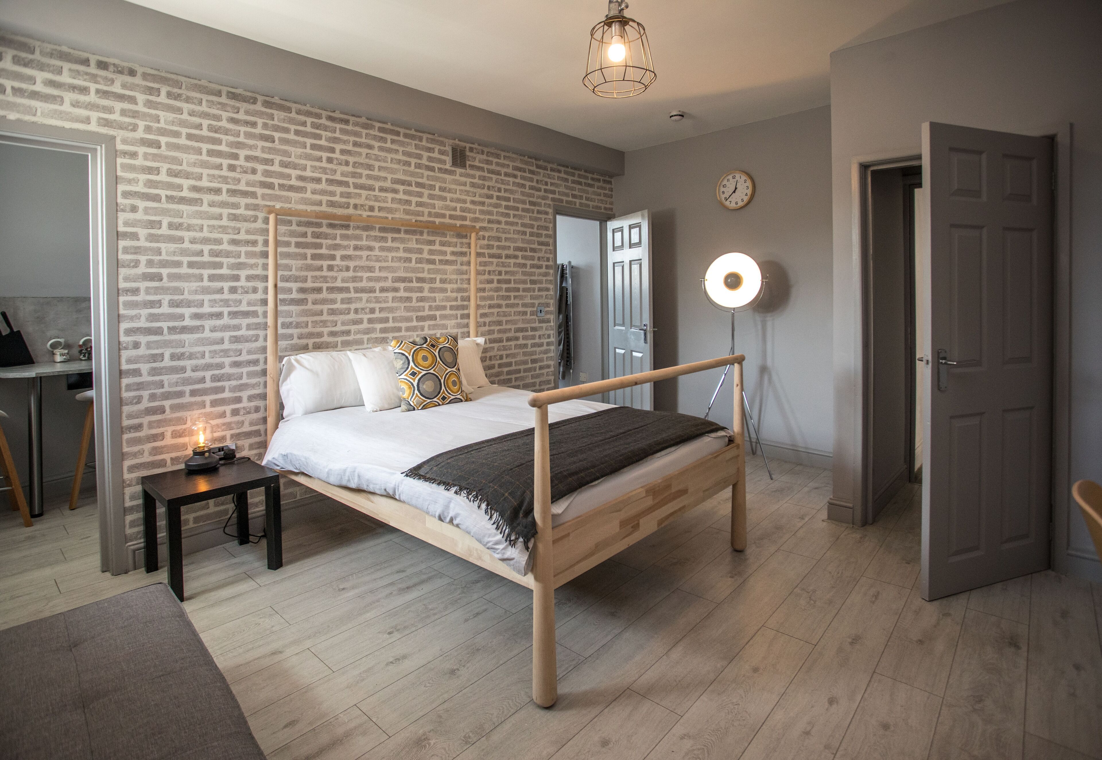 Un dormitorio con una cama de madera, una mesita de noche, un escritorio, un espejo, un reloj de pared y una puerta.