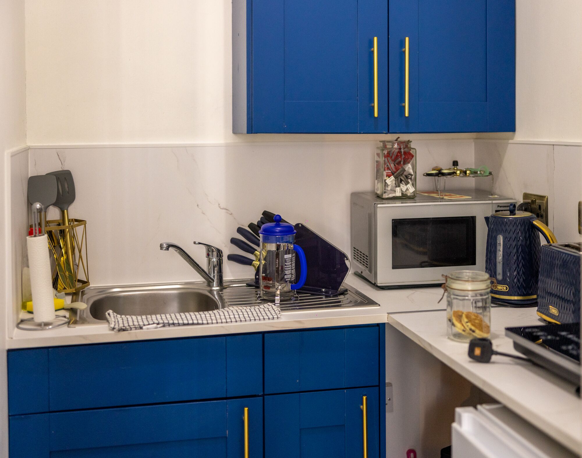 Una cocina con gabinetes azules, un microondas, una cafetera y varios utensilios.