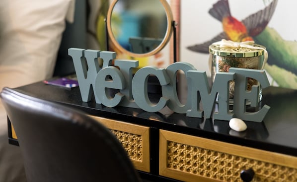 Un fauteuil en cuir noir, un miroir décoratif et une pancarte « BIENVENUE » sur une commode noire et dorée.
