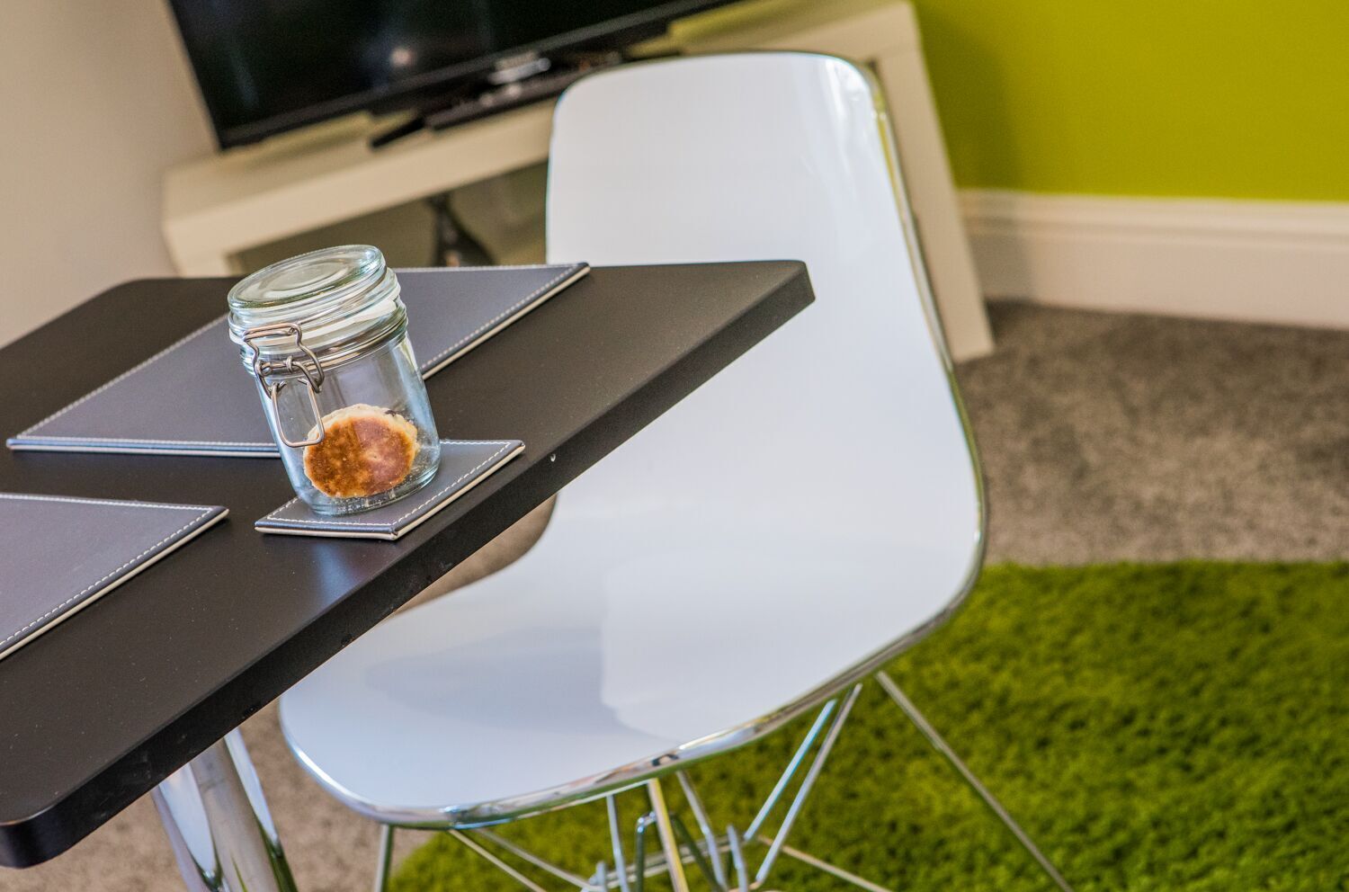 A table with a glass jar containing a brown substance, a black notebook, and a white chair.