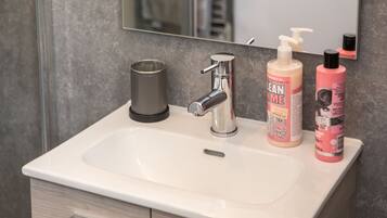 A bathroom sink with a modern faucet, a soap dispenser, and a bottle of shower gel.