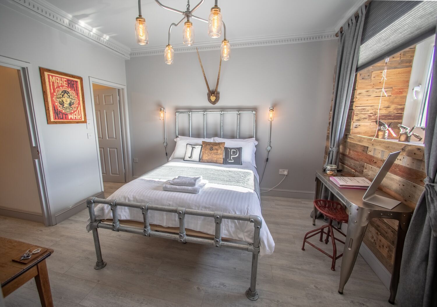 A bedroom with a metal-framed bed, a desk with a laptop, and a wooden wall.