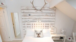 A bedroom with a bed, a bedside table, a lamp, a fan, and a wall-mounted deer head decoration. - James Place @ Dowlais (Merthyr Tydfil)