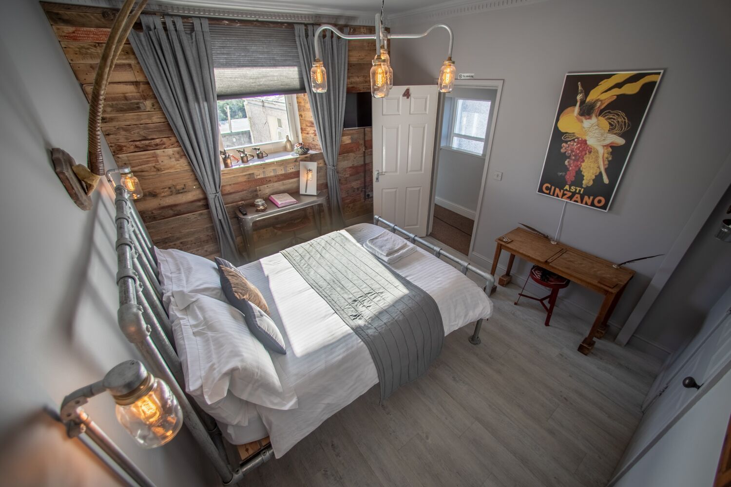 Un dormitorio con cama, un escritorio de madera, un espejo y una ventana con cortinas.
