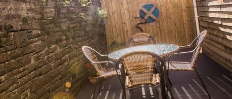 A patio with a round table and four wicker chairs, a wooden fence, and a stone wall.