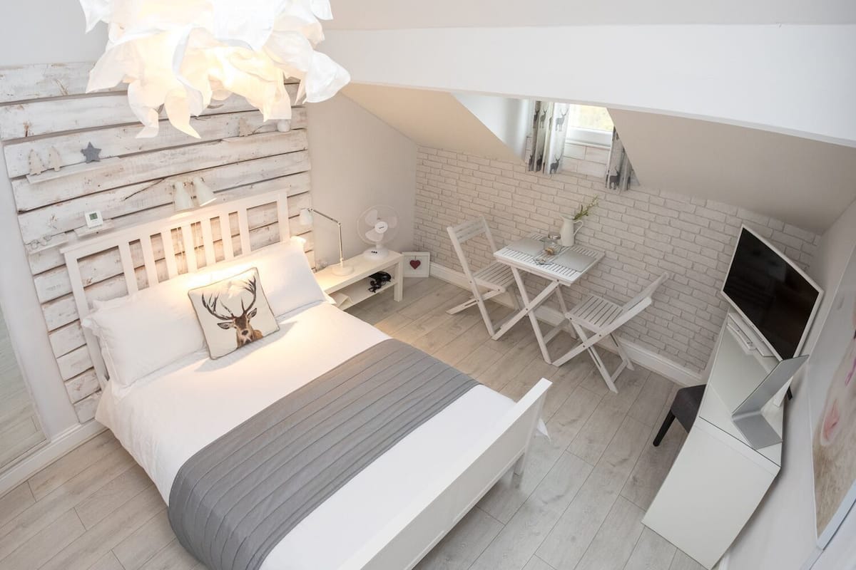 A bedroom with a bed, bedside table, lamp, chair, and a TV.