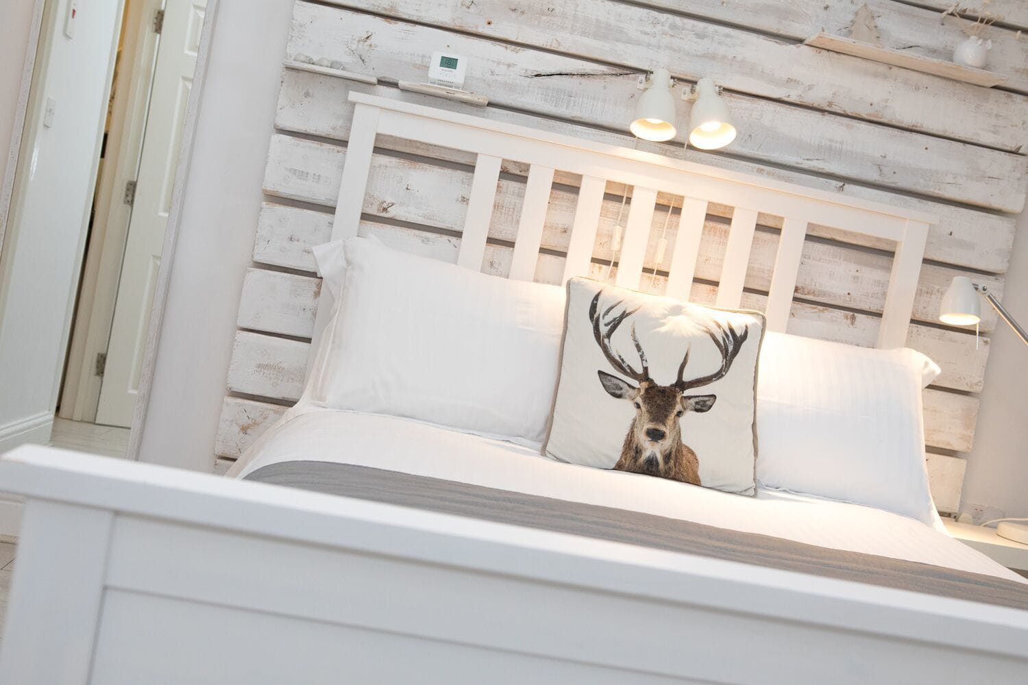 A bed with a white headboard, a pillow with a deer image, and a bedside lamp.